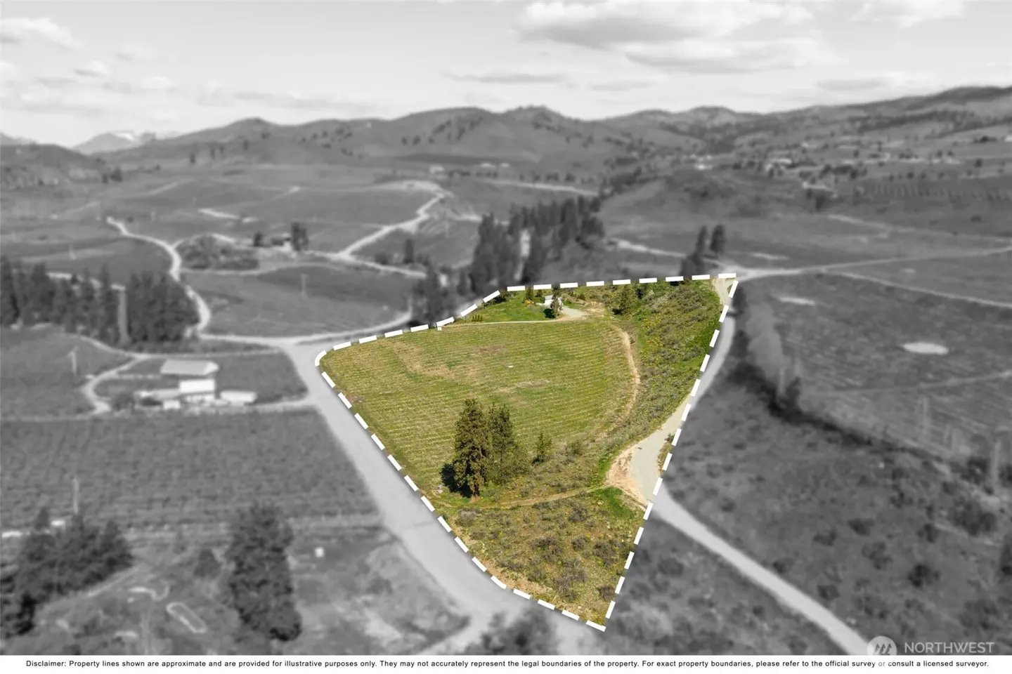 Aerial view of a green lot outlined in white, surrounded by a grayscale landscape of hills and roads.