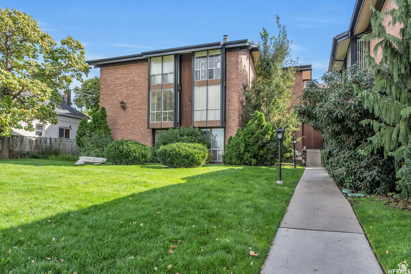 Two-story brick apartment building with large windows and a green lawn. A sidewalk leads to the entrance.