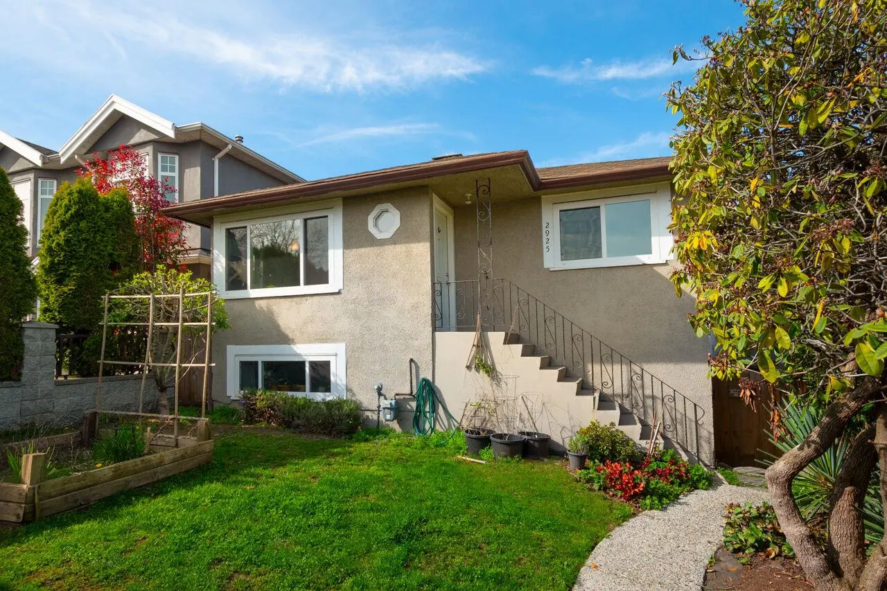 Tan two-story house with white trim, a small garden, and a stone walkway leading to the front door. Blue sky in the background.