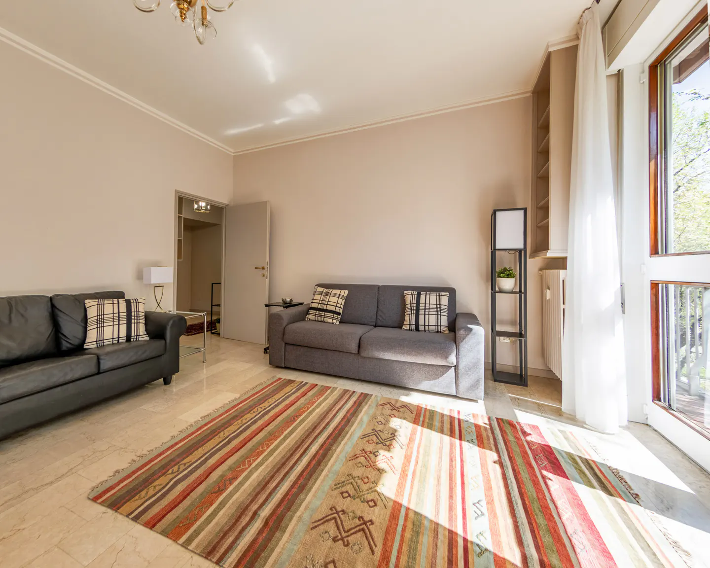 Living room with a black leather sofa, a gray sofa, and a colorful striped rug on a marble floor. A door leads to another room.