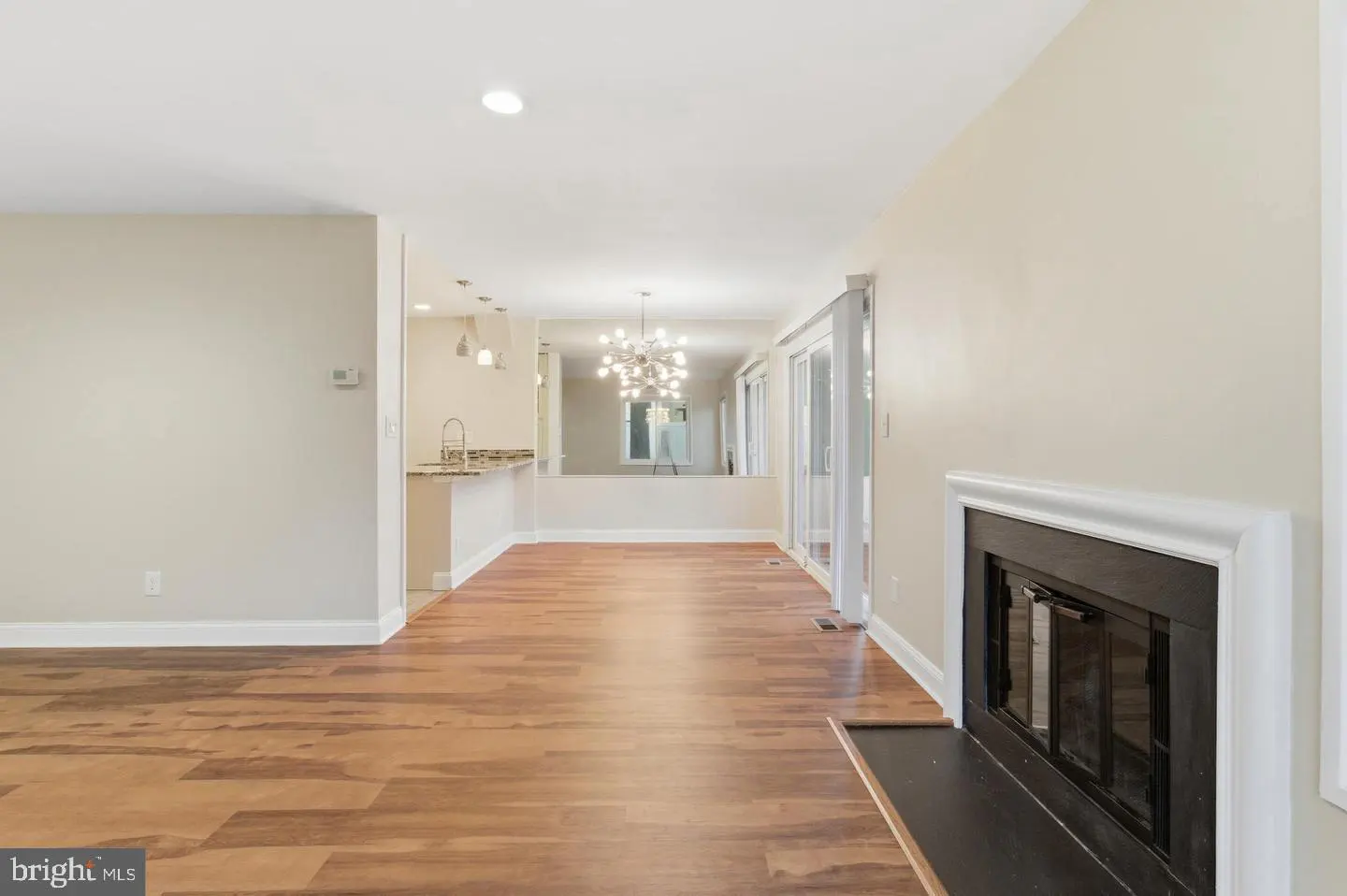 Bright, open-concept living space with wood floors, a fireplace, and a view into the kitchen and dining area. Neutral wall colors.