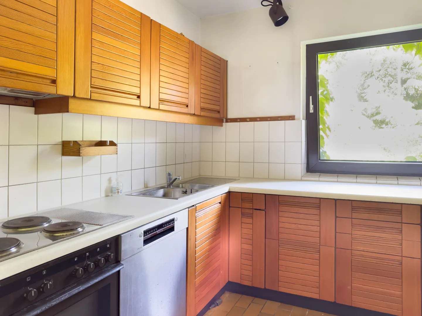 Kitchen with wooden slatted cabinets, white tiled backsplash, stainless steel sink, dishwasher, and a window.
