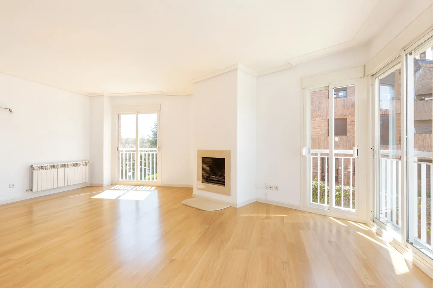 Bright, empty living room with hardwood floors, white walls, a fireplace, and balcony doors.