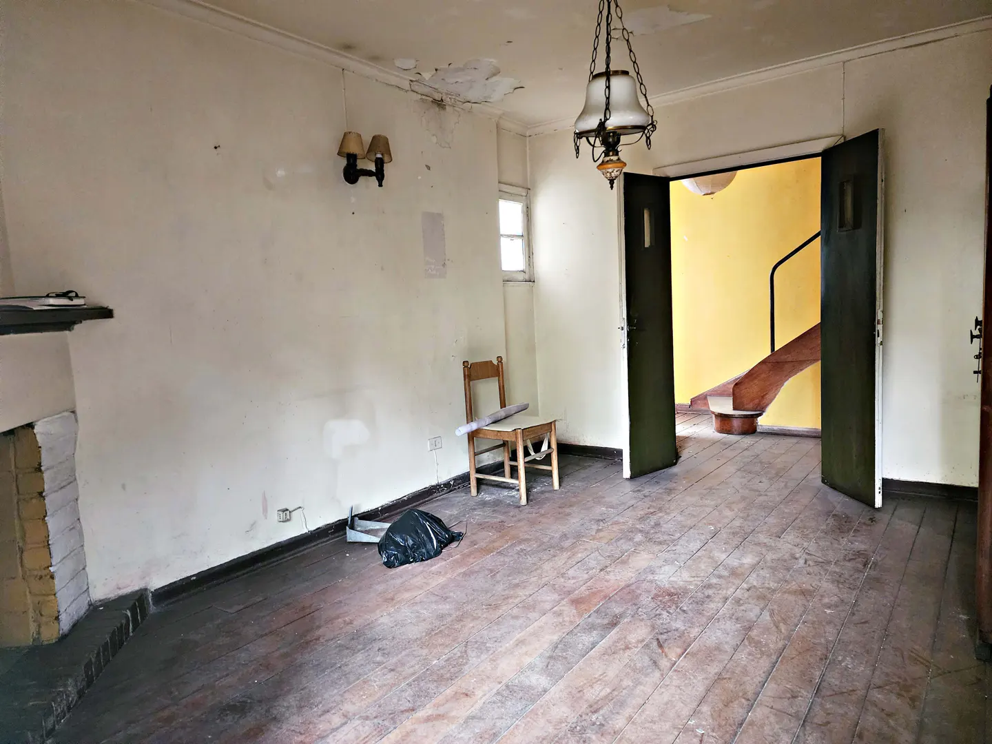 A vacant room with peeling paint, dark wood floors, and an open doorway to a yellow stairwell.