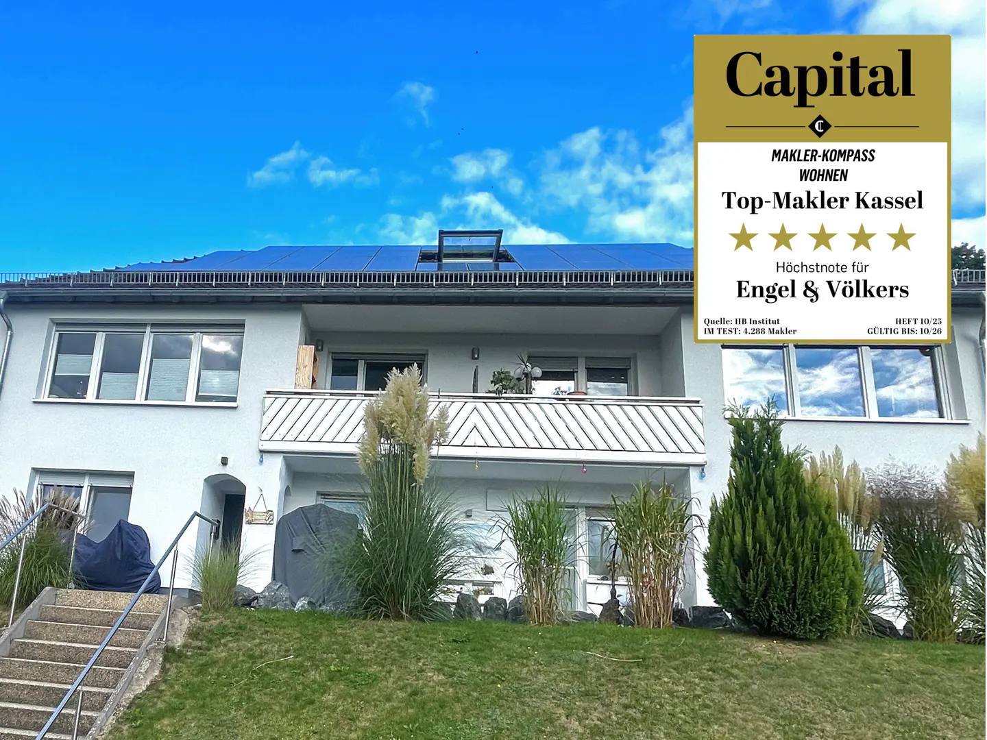 A two-story white house with solar panels on the roof under a blue sky. A "Capital" award is displayed on the right.