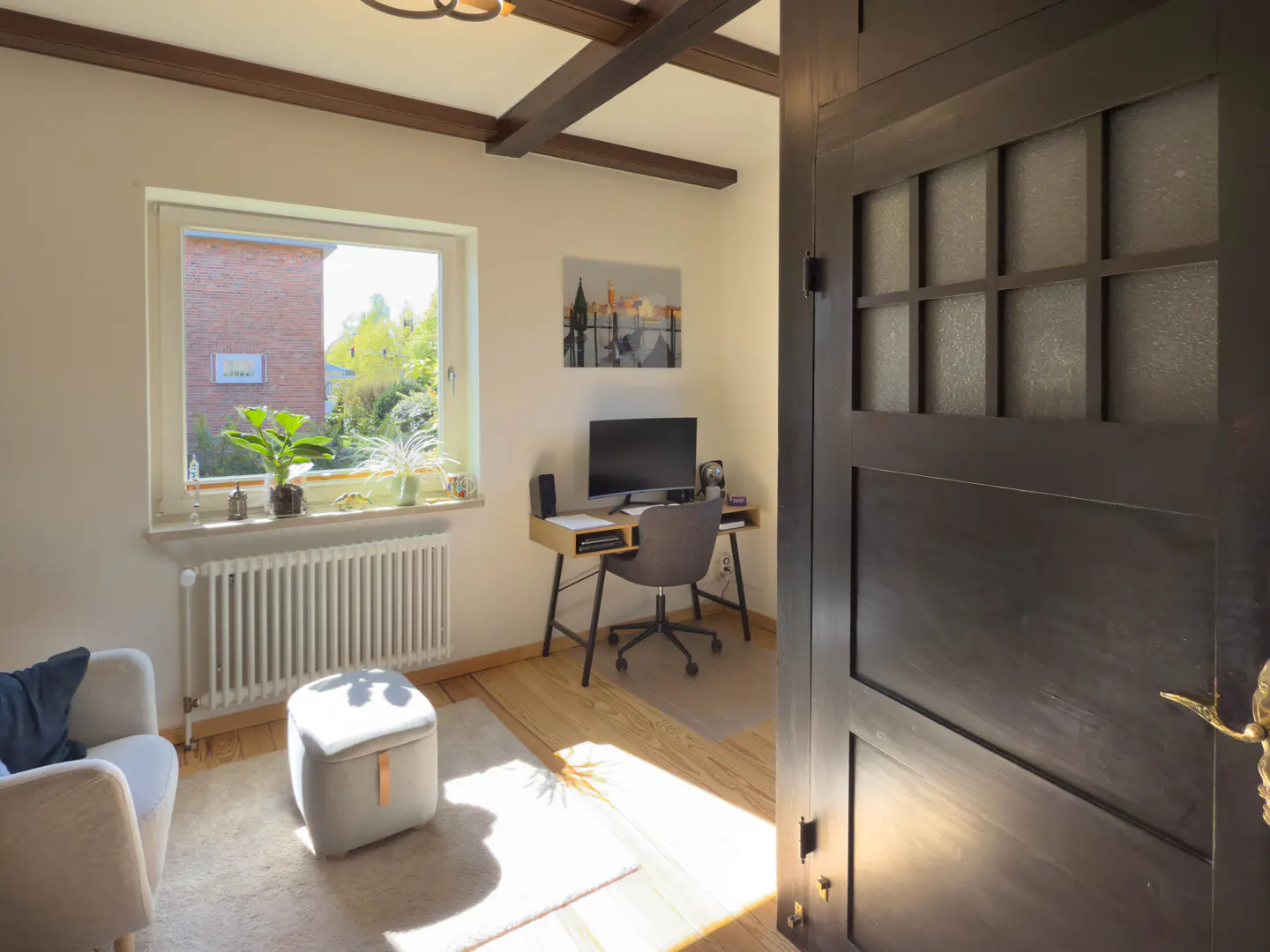 A bright home office with a desk, computer, chair, and window. A dark wood door is partially open on the right.