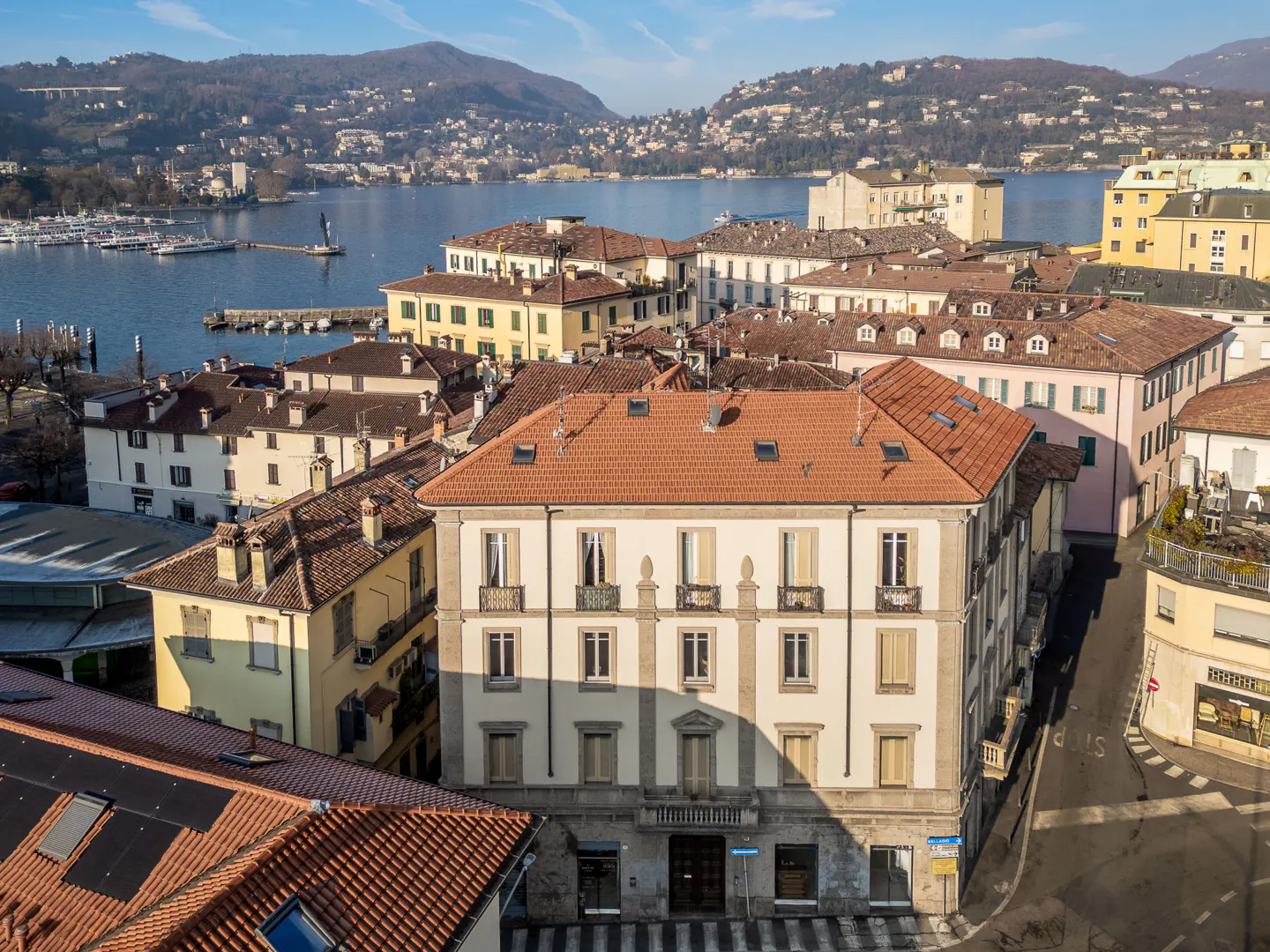 Aerial view of a European town with terracotta roofs, yellow buildings, and a lake with mountains in the background.