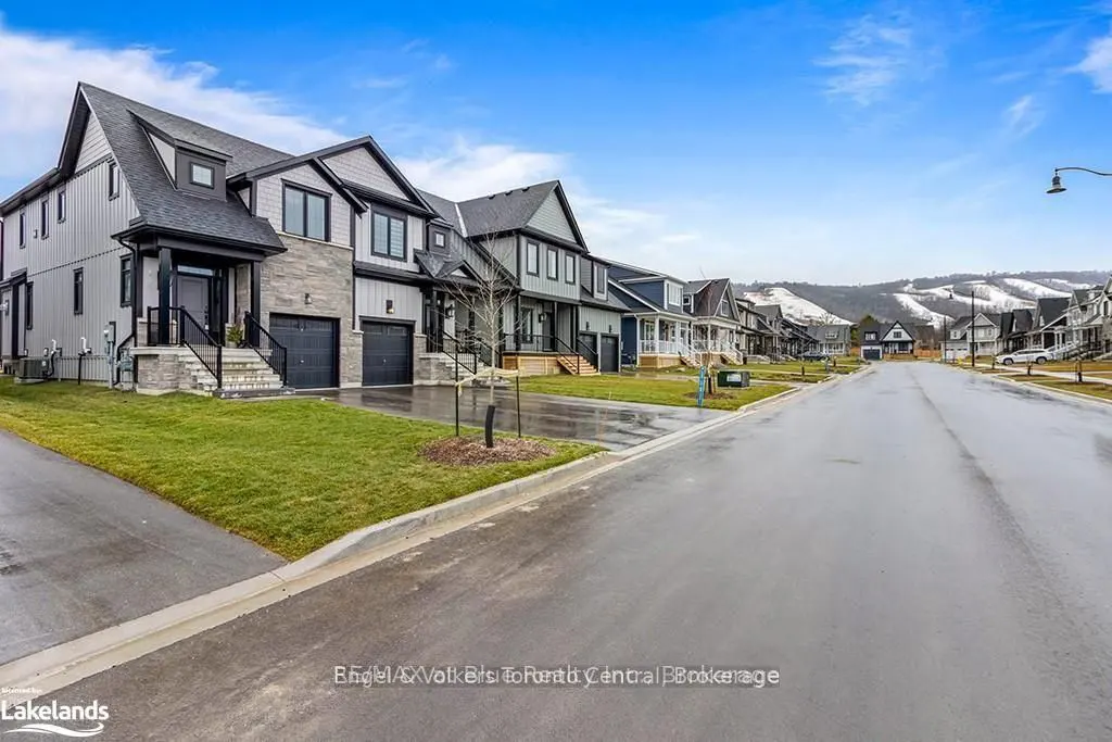 Street view of modern two-story homes with gray siding, black trim, and attached garages. Snowy hills are visible in the background under a blue sky.