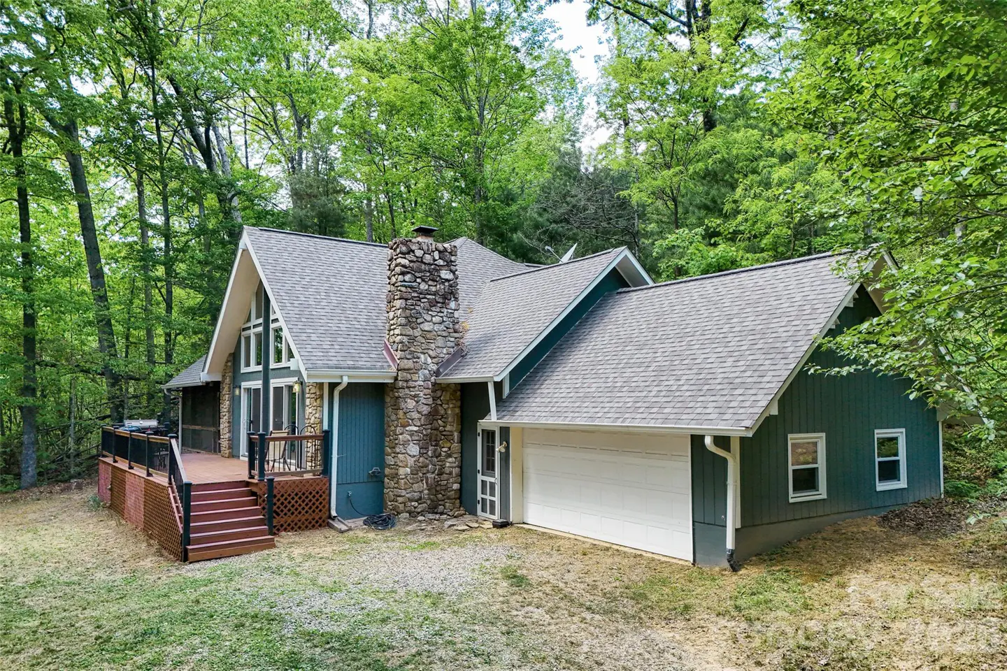A-frame house with a stone chimney, gray roof, and blue and green siding, surrounded by trees.