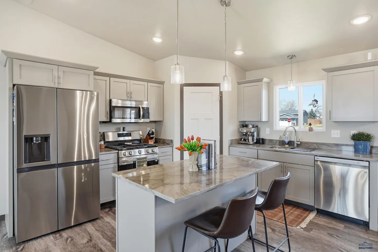 Bright kitchen with gray cabinets, stainless steel appliances, and a marble-topped island with two stools.