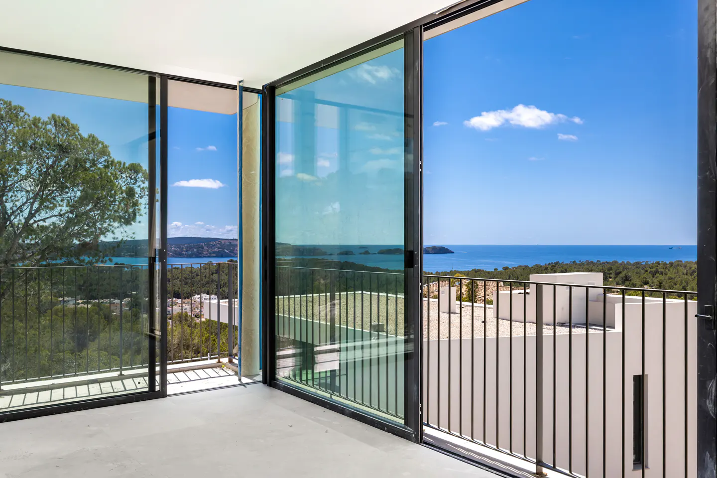 View from a modern home with sliding glass doors opening to a balcony overlooking the ocean and islands on a sunny day.