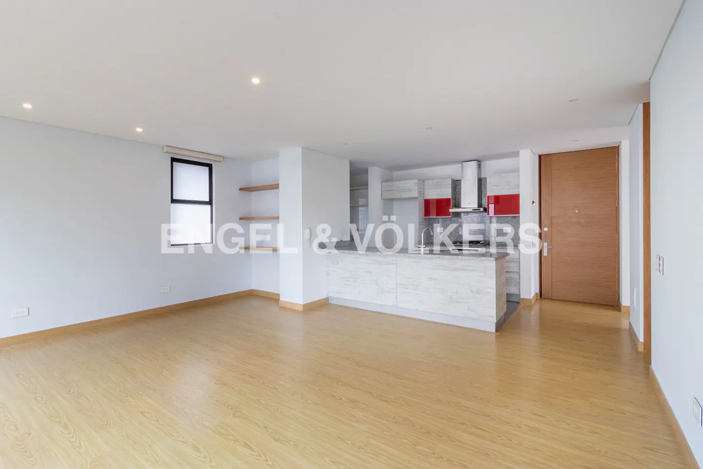 Modern open-plan living area with light wood floors, white walls, a kitchen island, and a wooden door.