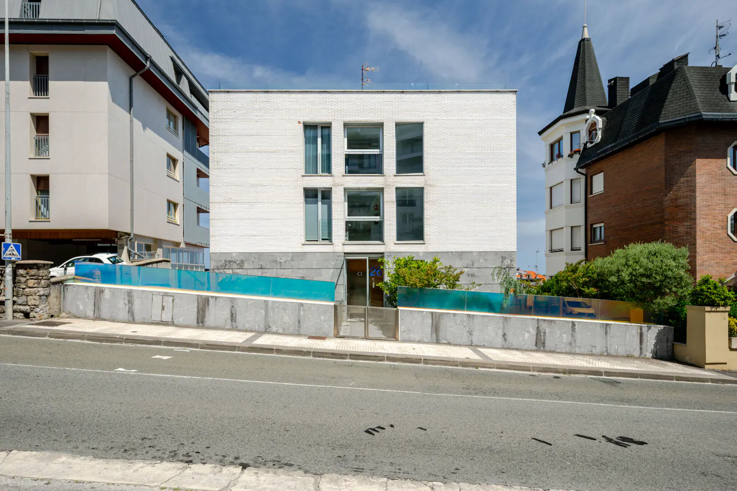 A modern, white brick building with large windows sits on a raised concrete platform with a blue glass barrier.