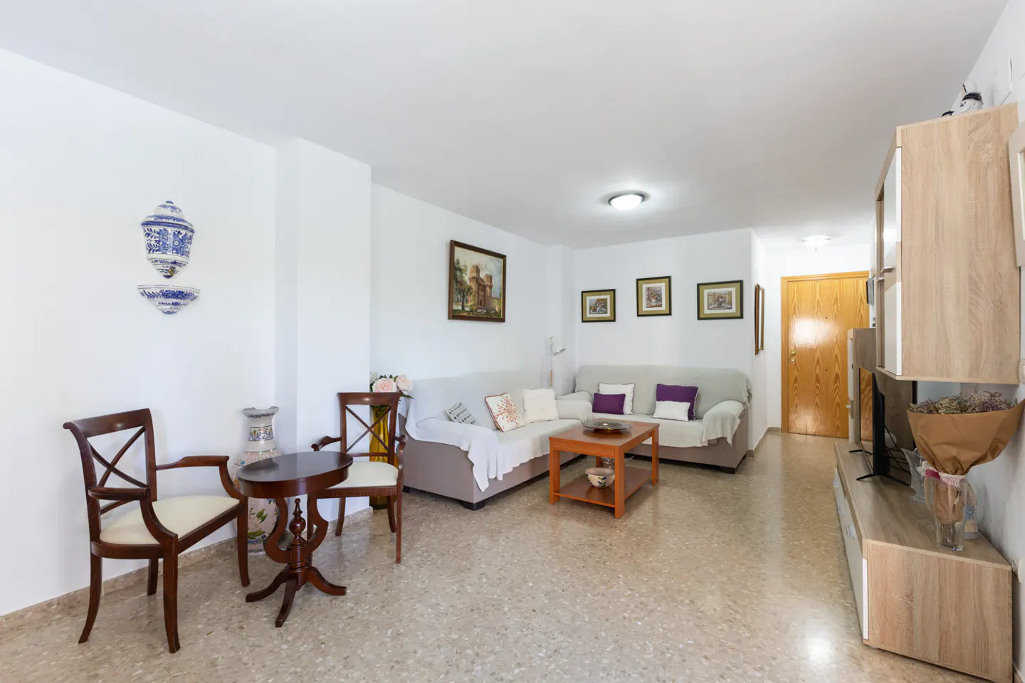 Bright living room with white walls, beige sofas, wood furniture, and decorative wall art.
