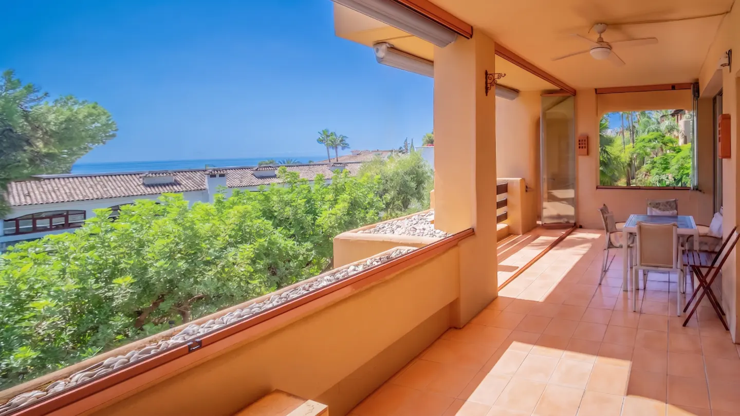 Covered patio with tile floor, table and chairs, and a view of the ocean and trees.