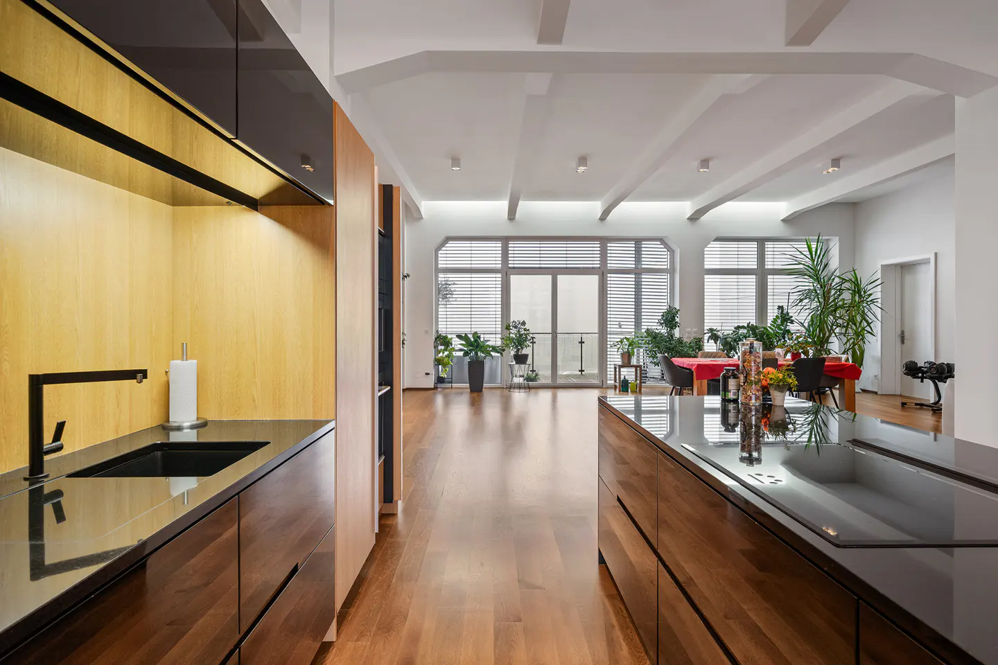 Modern kitchen with wood cabinets, black countertops, and stainless steel appliances. Large windows provide natural light.