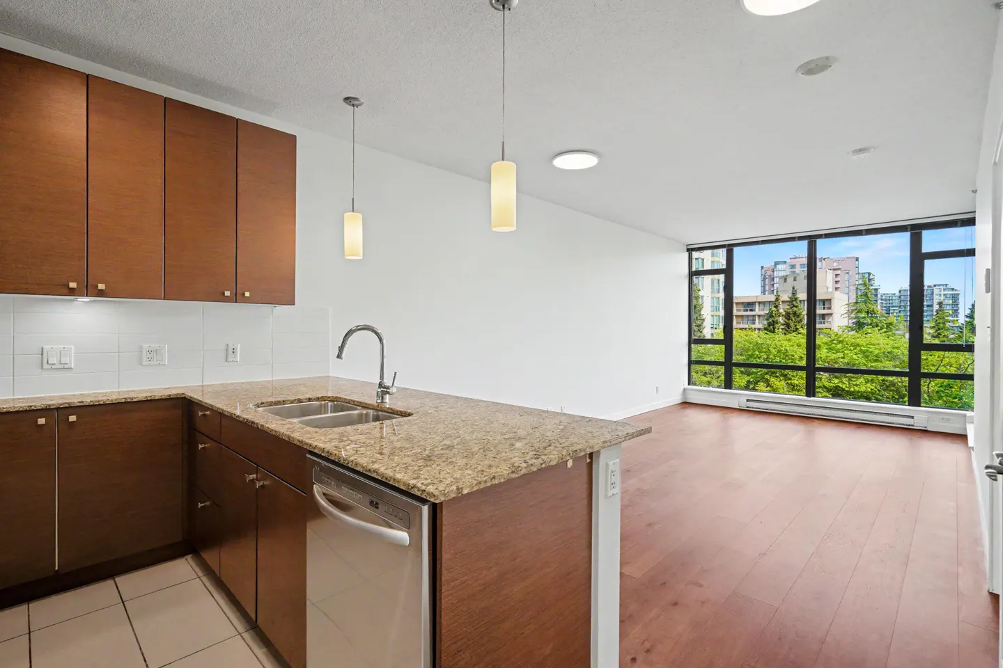 Bright, modern condo interior with brown cabinets, granite countertops, stainless steel appliances, and a large window with a city view.