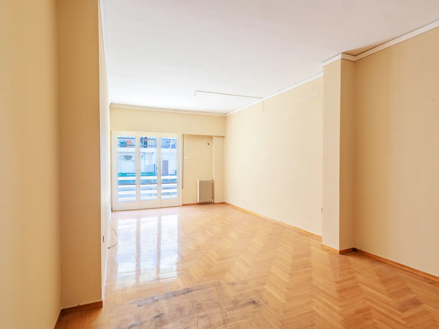 Empty room with herringbone wood floor, beige walls, and white trim. Glass doors lead to a balcony.