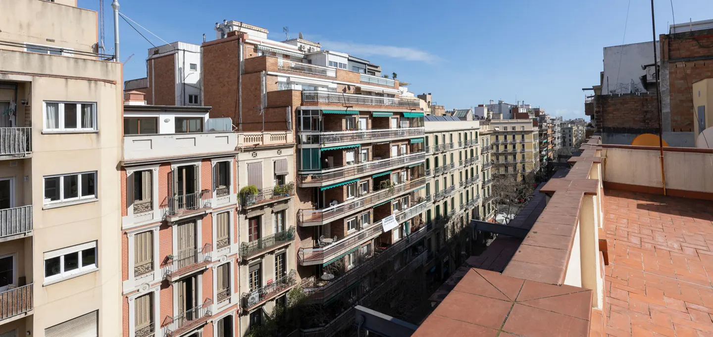 View from a rooftop overlooking a street in Barcelona, Spain, with tall buildings and a blue sky.