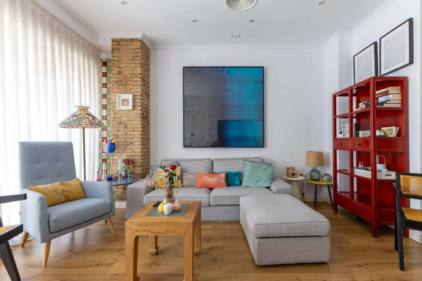 Living room with a gray sofa, blue armchair, wooden coffee table, and red bookshelf on a wood floor.