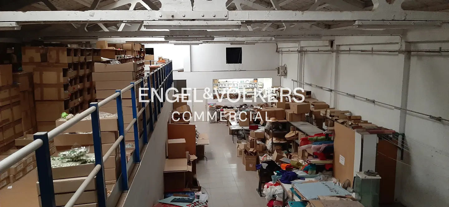 Interior view of a commercial warehouse space filled with boxes and storage, with white walls and a high ceiling.
