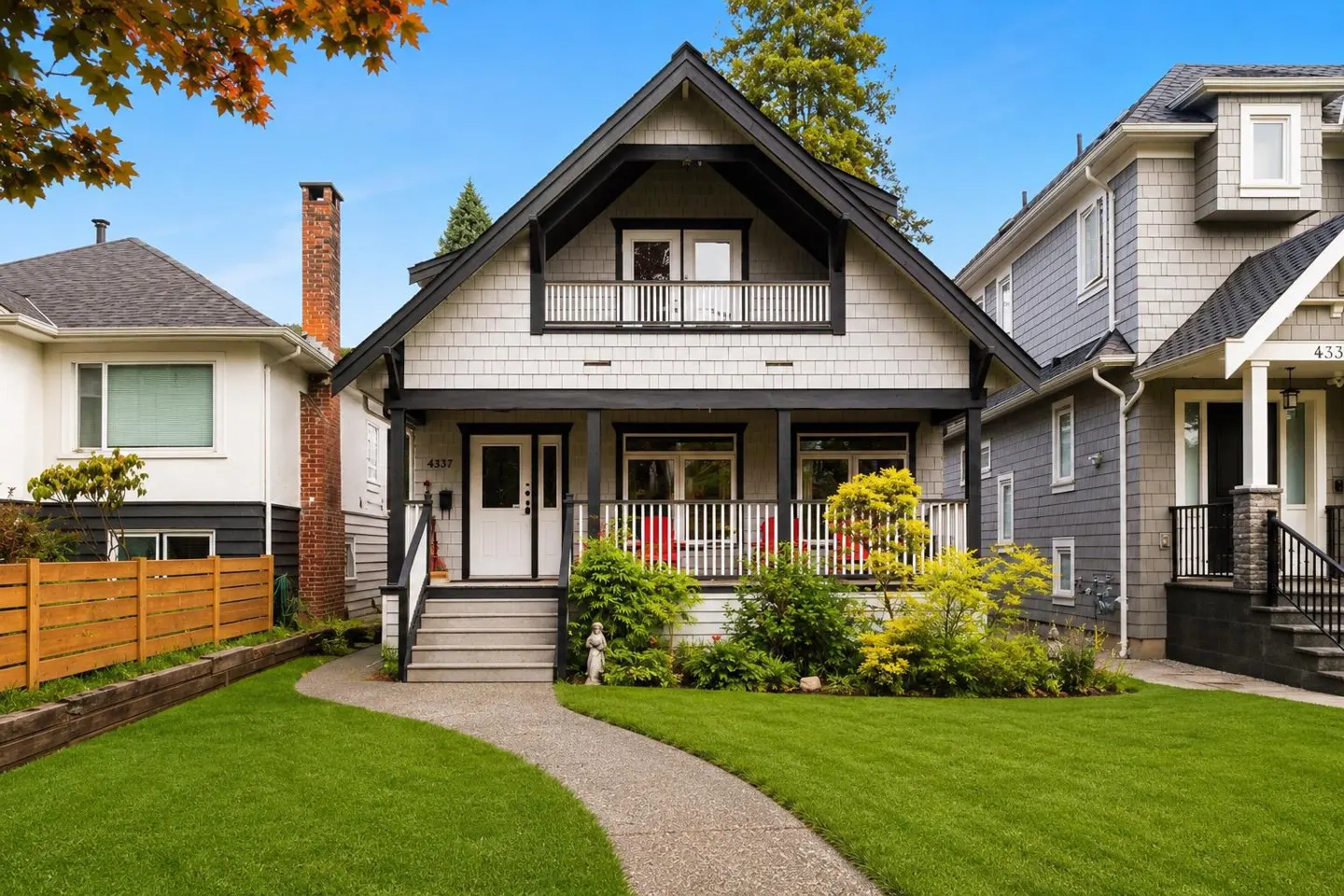 Two-story house with gray shingles, black trim, white door, and a small porch with red chairs. A stone path leads to the house.