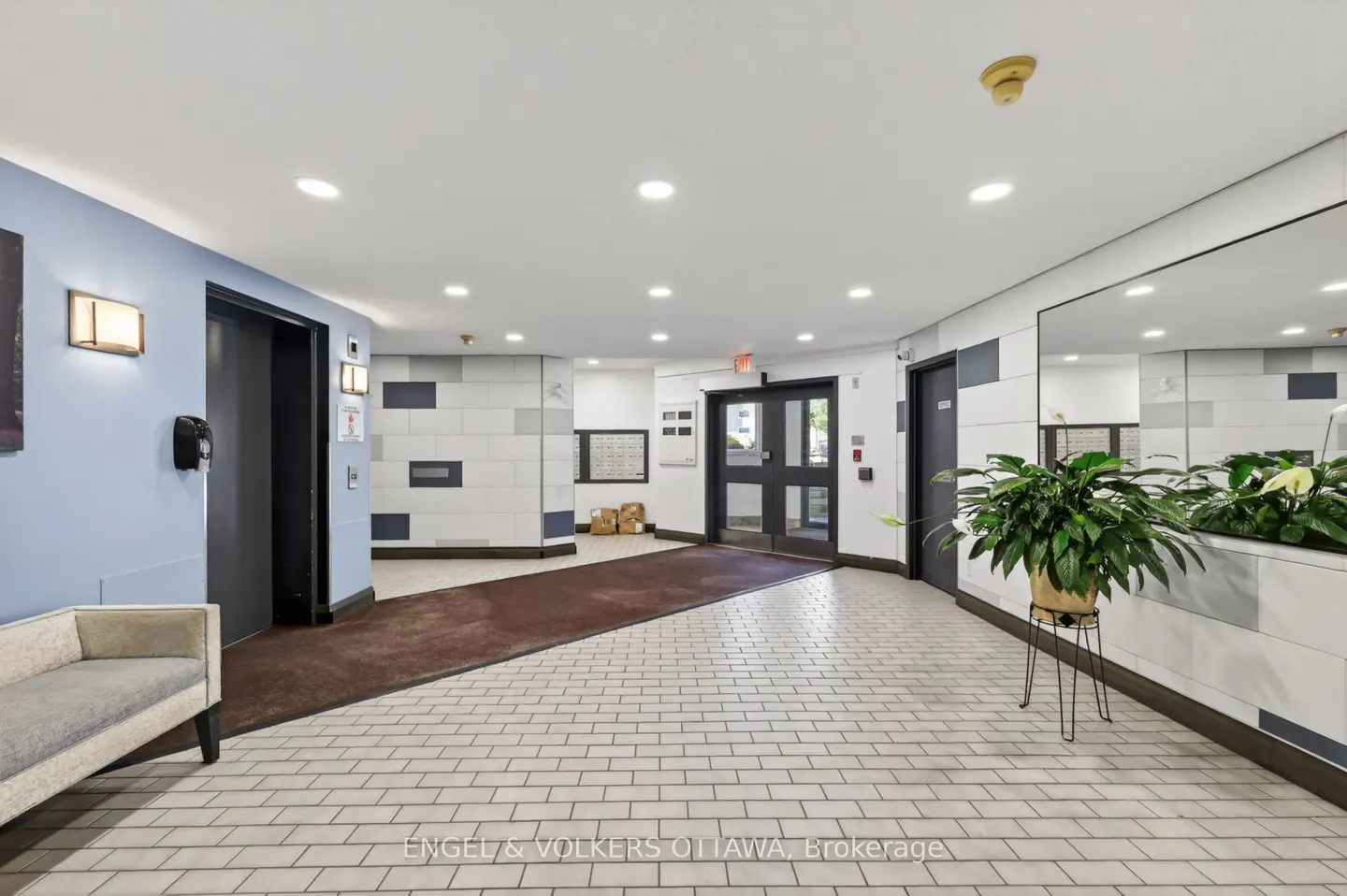 Bright apartment building lobby with a light blue wall, tiled floor, elevator, glass entrance doors, and a potted plant.