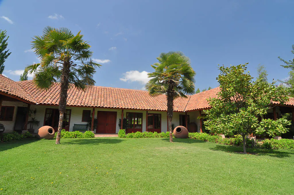 Exterior of a white house with a red tile roof, green lawn, and palm trees under a blue sky.