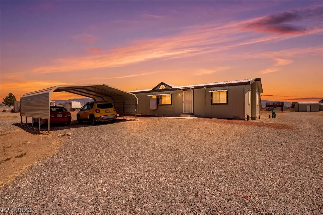 Exterior of a single-story home with a gravel yard at sunset. A carport shelters a red sedan and yellow SUV.