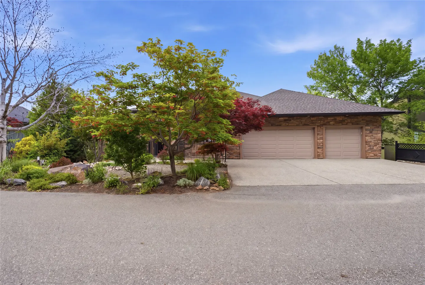 A single-story house with a two-car garage, stone accents, and landscaping under a blue sky.