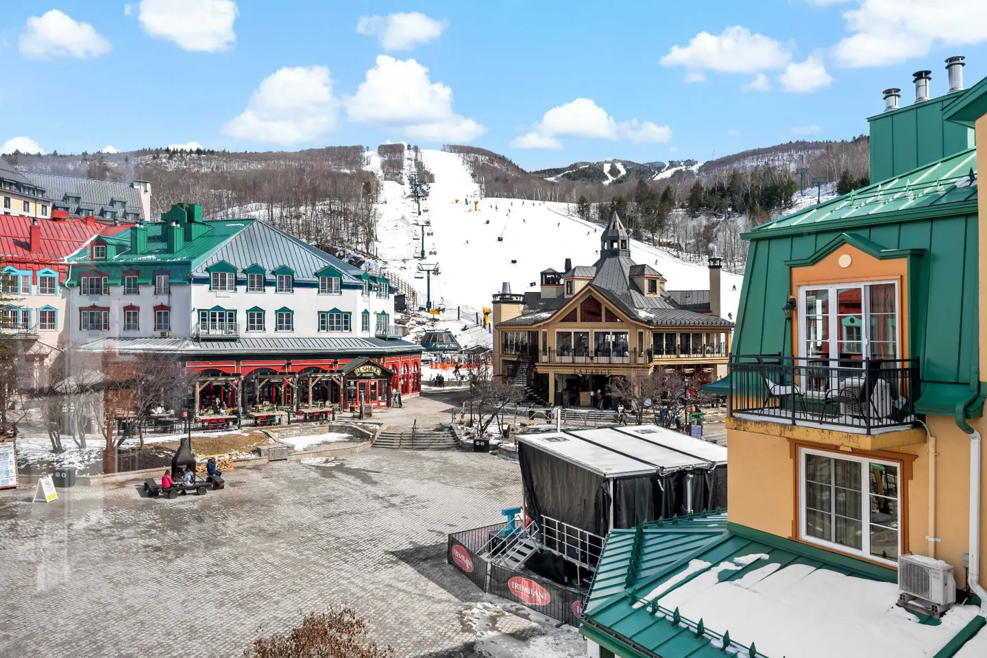 View of a ski resort village with colorful buildings, a ski slope, and a blue sky.