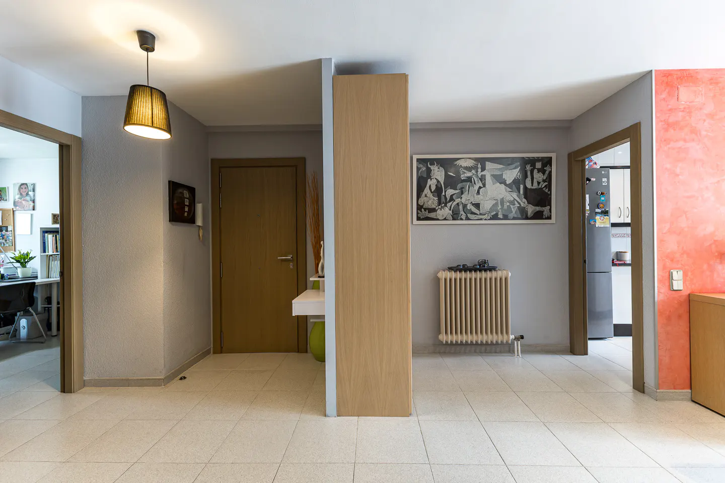 Hallway with light tile floors, a central wooden pillar, a hanging lamp, a radiator, and doorways to other rooms.