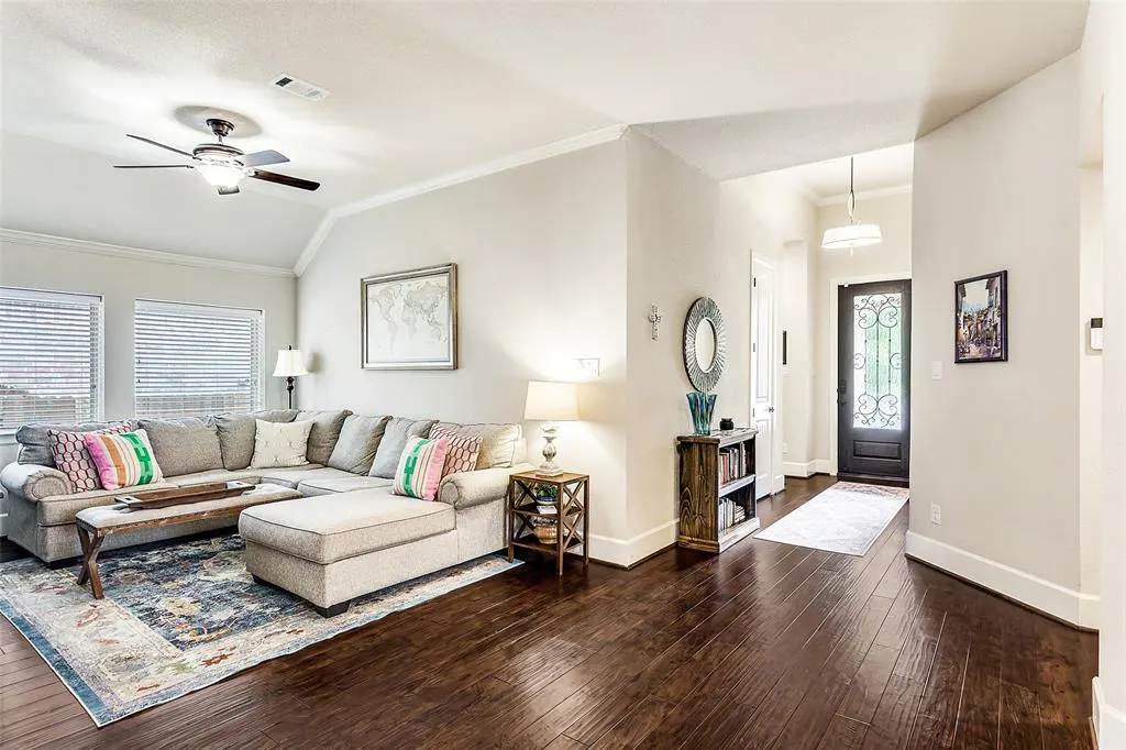 A bright living room with a gray sectional sofa, wood floors, and a front door visible in the background.