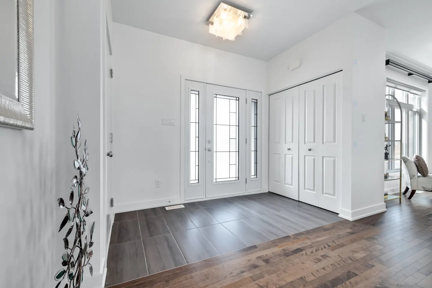 Bright entryway with white walls, a front door with glass panes, and a closet. The floor is a mix of gray tile and wood.