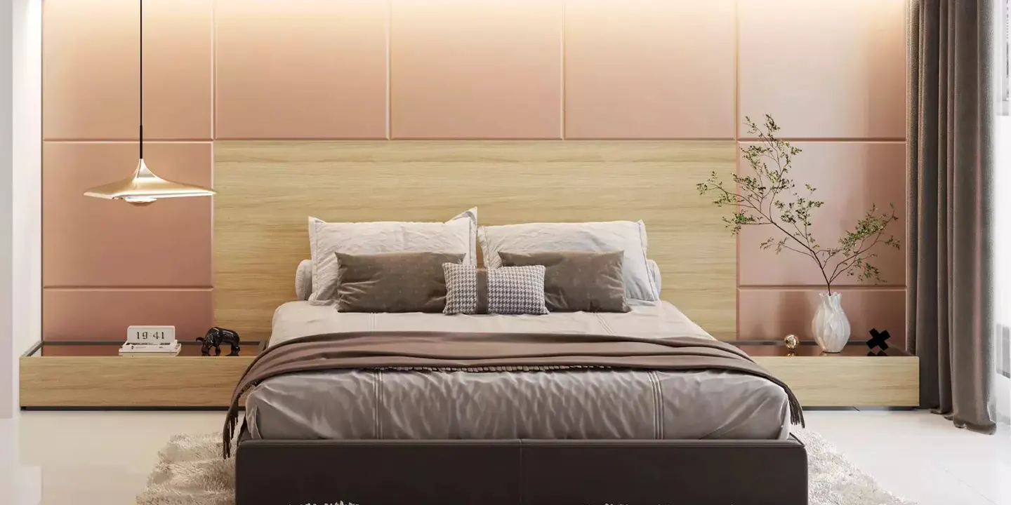 Bedroom with a brown bed, pillows, and a blanket. There is a wooden headboard and a pink wall behind the bed. A gold lamp hangs on the left side.
