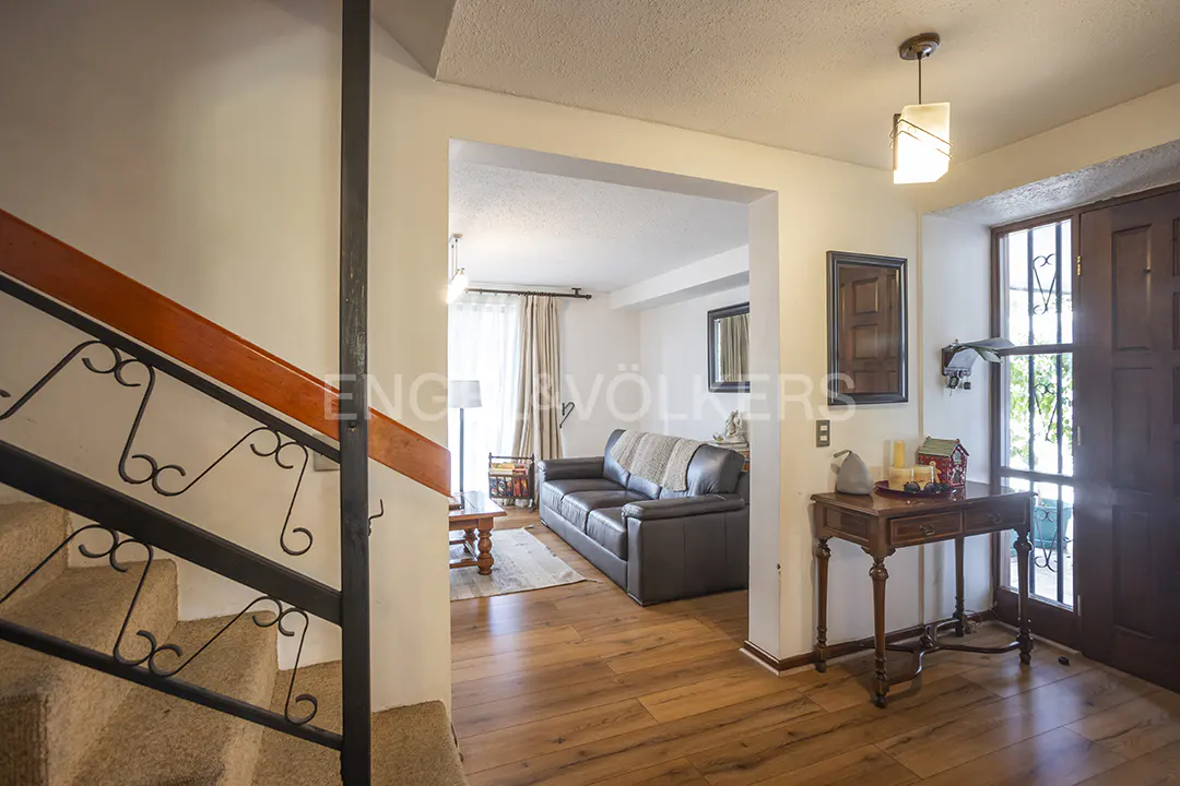 A home's entryway with a staircase, wooden floors, and a living room visible through an archway.