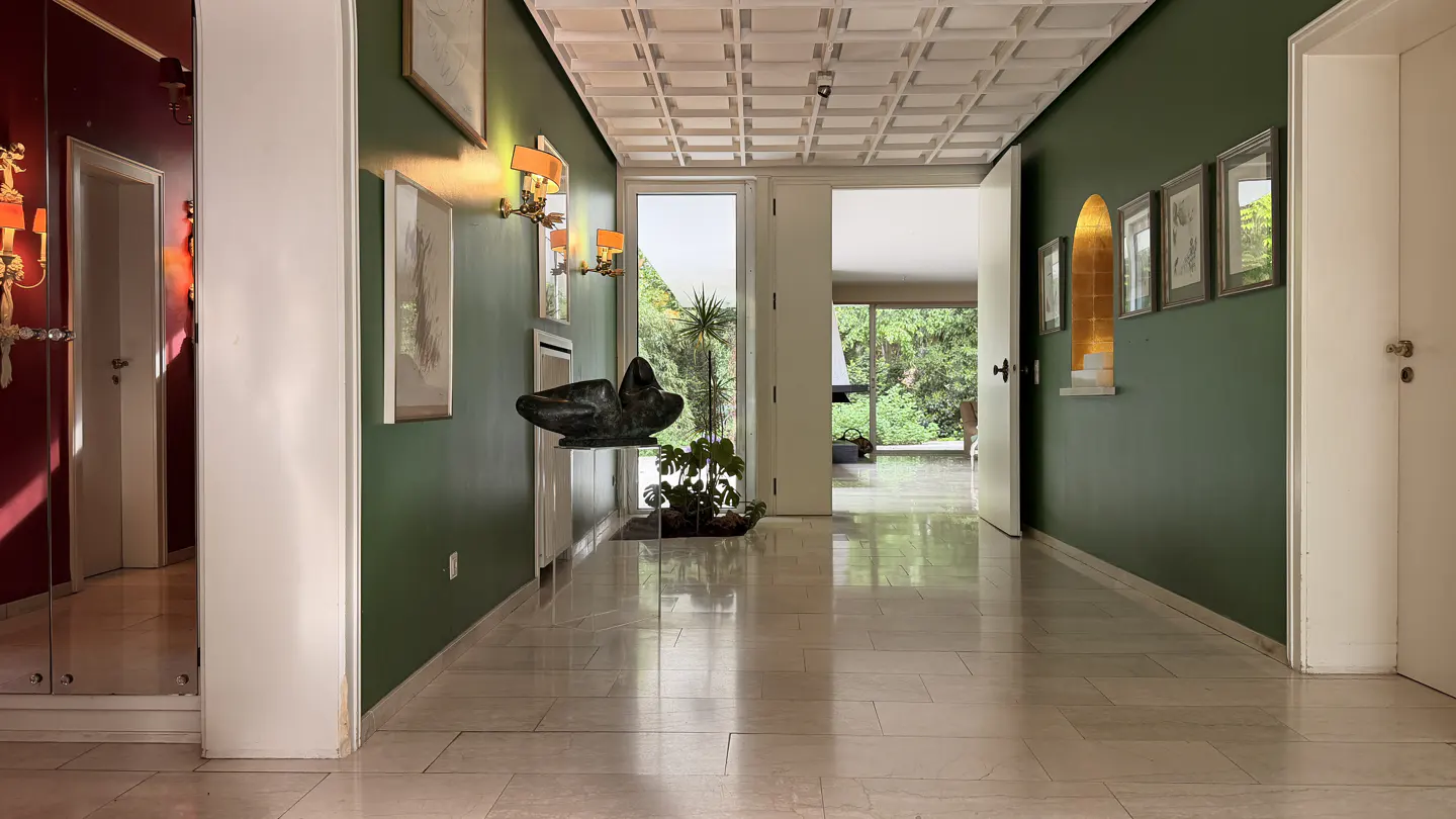Hallway with green walls, marble floors, and white doors. Artwork and sconces adorn the walls. A sculpture sits on a clear stand near the entrance.