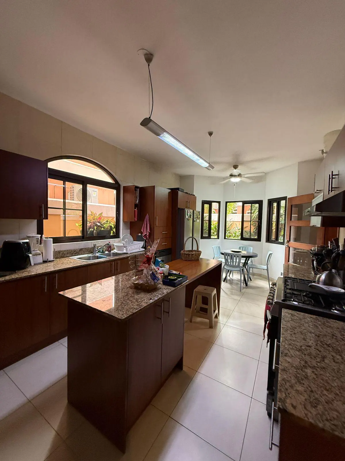 A bright, open kitchen with brown cabinets, granite countertops, and a central island. A dining area is visible in the background.