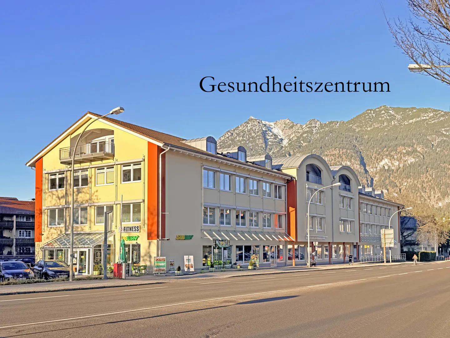 A three-story building with a yellow and orange facade, a Subway restaurant, and mountains in the background.