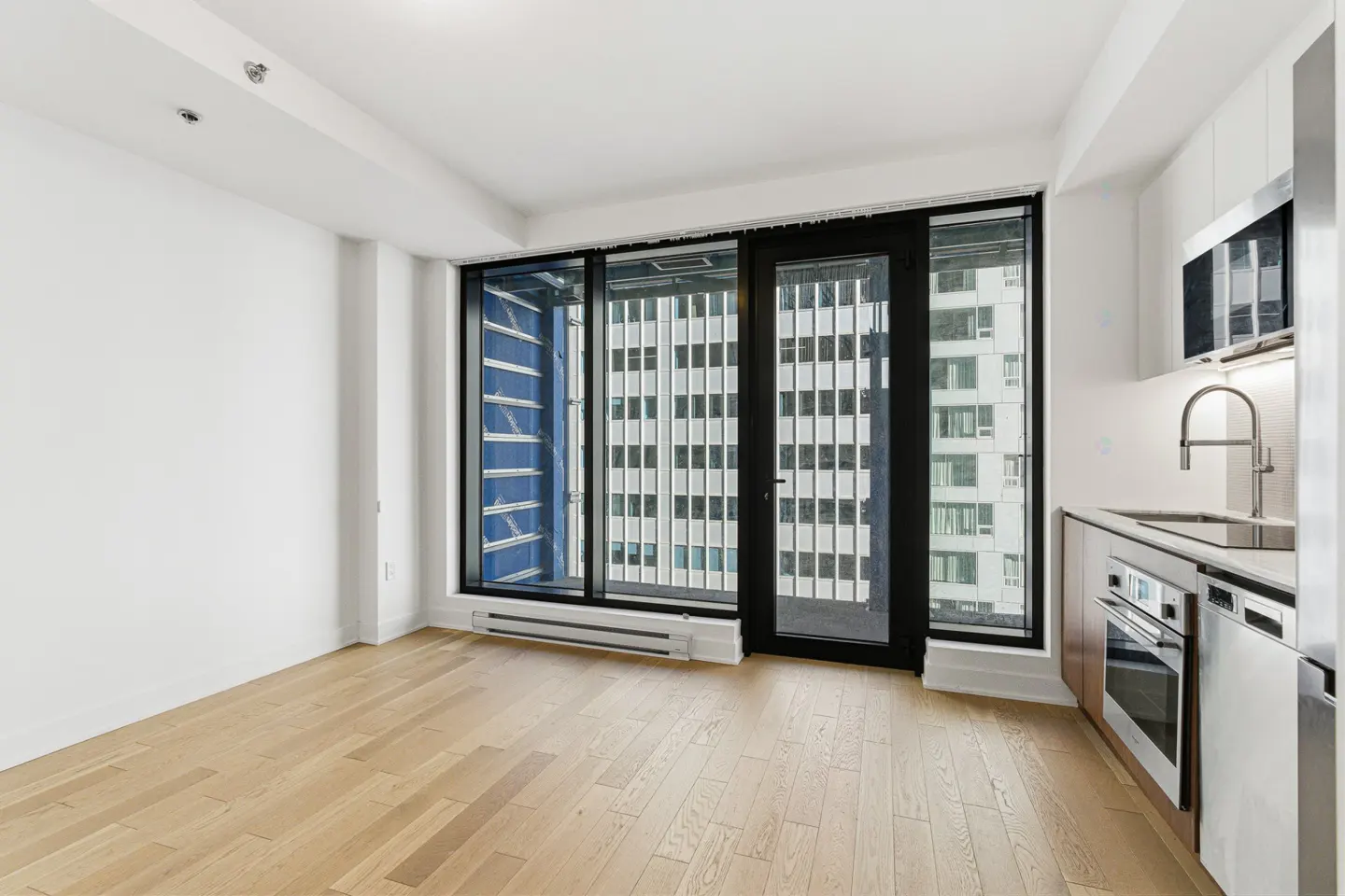Modern apartment with light wood floors, white walls, and a sleek kitchen, featuring floor-to-ceiling windows and a balcony.