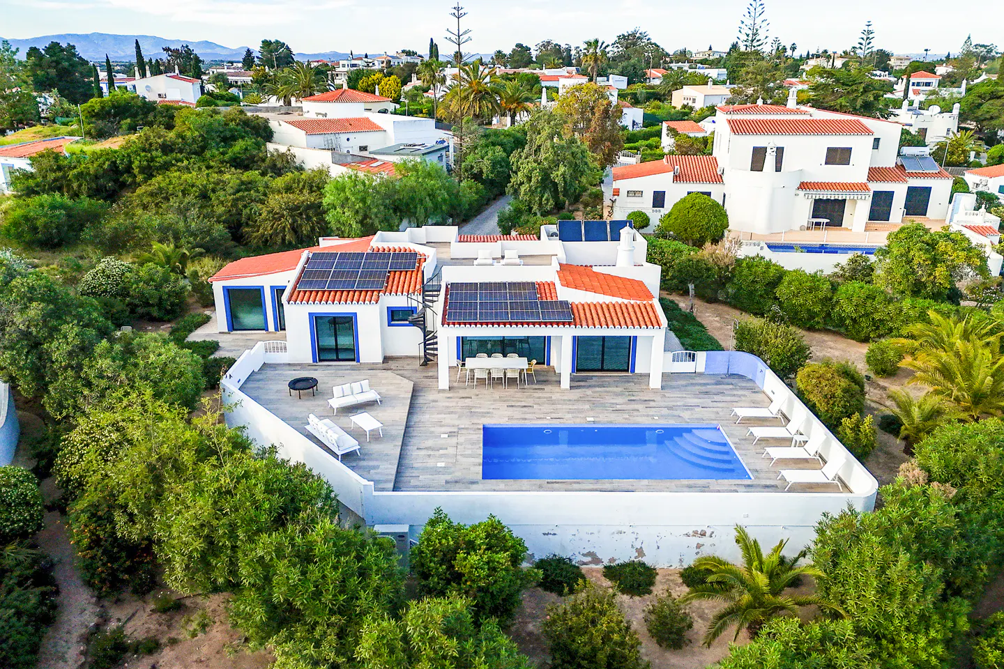Aerial view of a white house with a red tile roof, solar panels, a pool, and patio furniture.