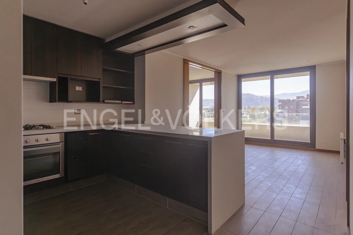 A modern kitchen with dark wood cabinets, a white countertop island, and large windows with a city view.