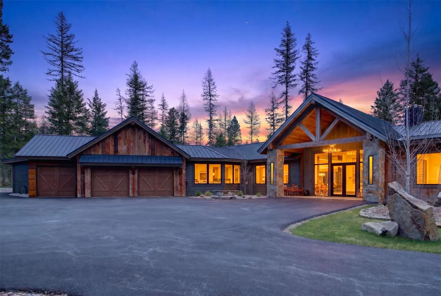 Exterior of a luxury home with a three-car garage, stone accents, and a large driveway at dusk.