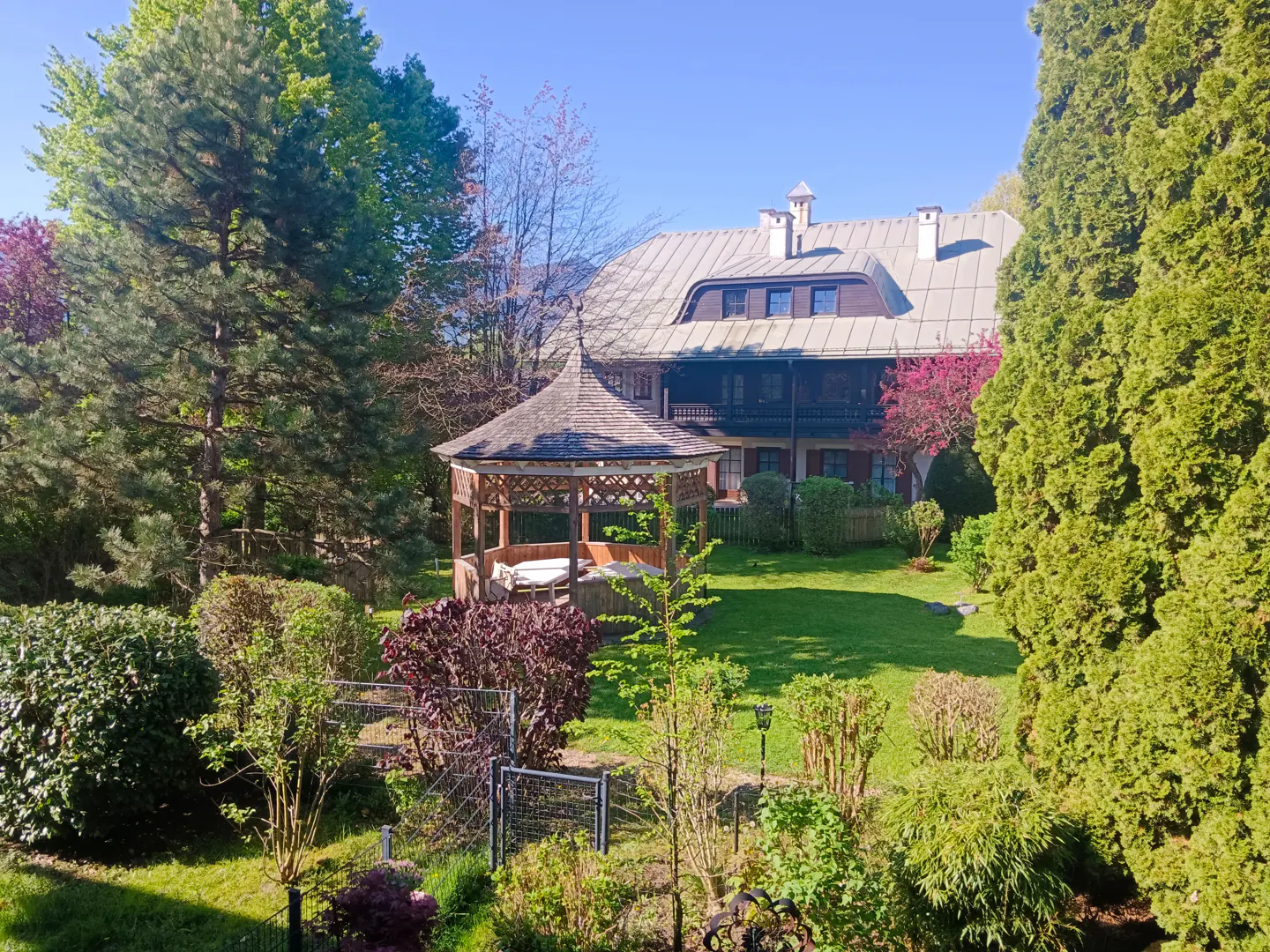 A house with a gazebo in a green garden on a sunny day.