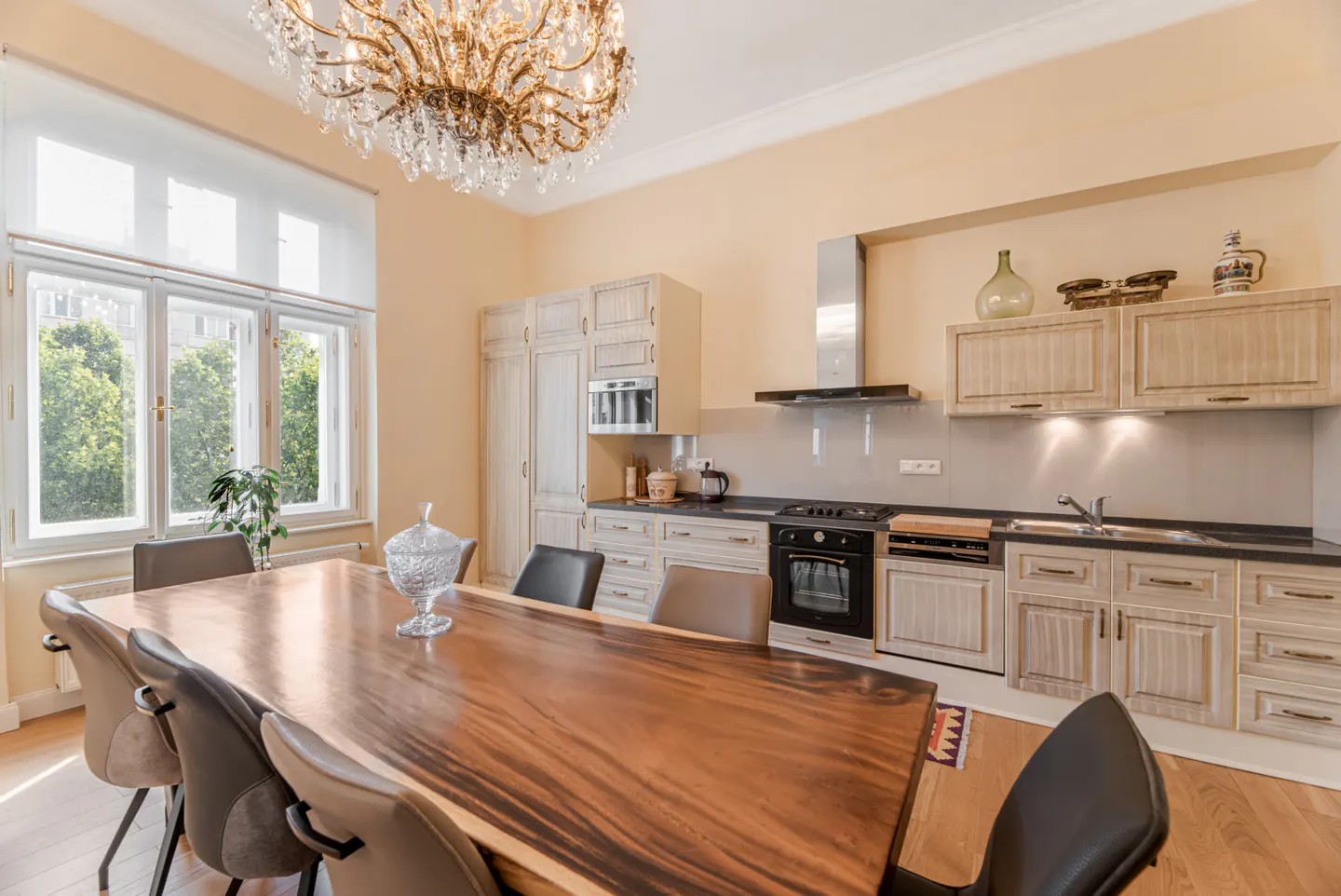 A bright kitchen with a large wood table, chairs, and a crystal chandelier.