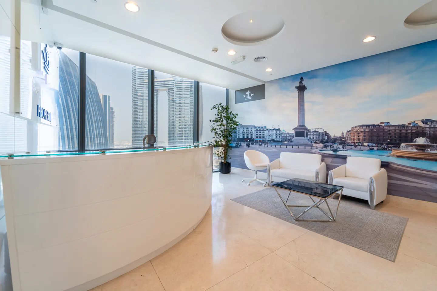 Modern office lobby with a white reception desk, city view, and London-themed wall art. White chairs and a glass table create a welcoming space.