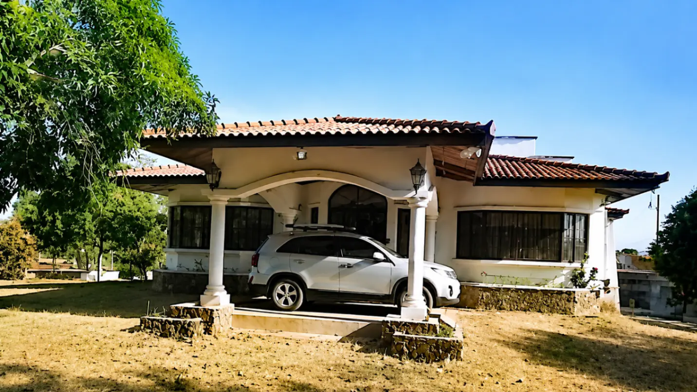 A white house with a red tile roof and a white car parked in the driveway.
