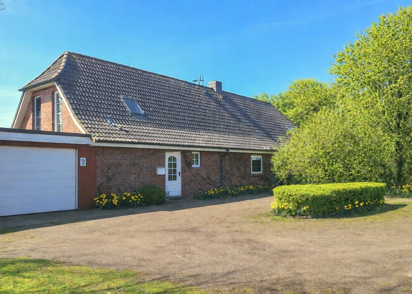 Exterior view of a brick house with a gray tiled roof, white door, and a white garage door on a sunny day.
