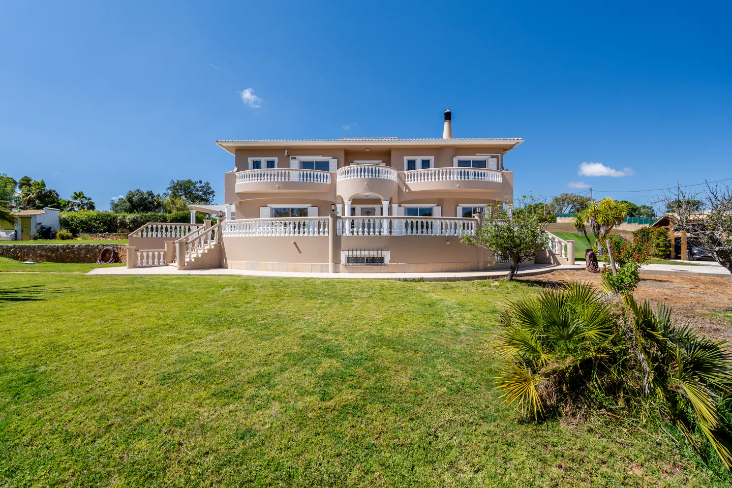 Two-story tan house with white balconies and a green lawn under a blue sky.