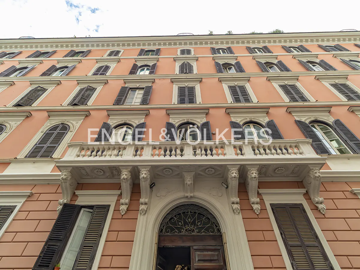 Exterior of a peach-colored building with dark shutters and a white balcony with lion head supports.